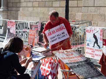 Un hombre con un letrero de derechos de los animales colgándole del cuello y muchos otros letreros de derechos de los animales alrededor de él