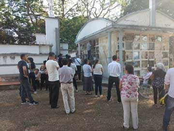 A man putting cement over the lid of a grave on a wall. Some people are staring