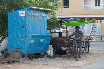 A man wearing a mask next to a bicycle-wheel-cart and a closed selling booth