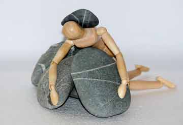 A wooden dummy lying on top of some stones with a stone on its back