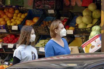 2 girls wearing masks in front of a vegetable and fruit shop