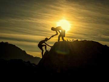 A man helping another one climb a mountain