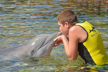 A boy on the water, kissing a dolphin