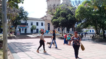 Some people passing by wearing masks. At the background, the word 'Garzón' in big colorful letters and a church