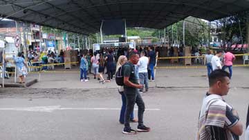 Un campo deportivo cubierto, con muchas personas adentro. Personas están pasando por la calle