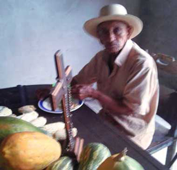 Don Joselito Cuellar Chacón with a hat, looking at the camera. He's having breakfast